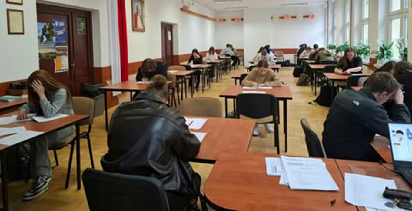 Zdjęcie przedstawia uczestników i uczestniczki etapu szkolnego Olimpiady Języka Angielskiego pogrążonych w pracy nad testem.