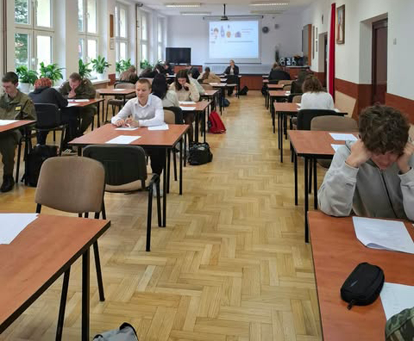 Zdjęcie przedstawia uczniów i uczennice piszące w sali test podczas pierwszego etapu szkolnego Olimpiady Języka Angielskiego.